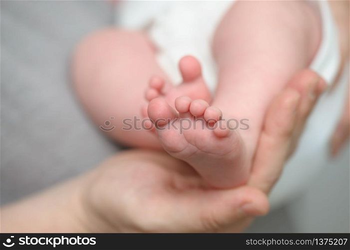 Mothers hands holding little newborn baby feet, macro closeup, selective focus. Mothers hands holding newborn baby feet