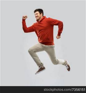 motion and people concept - smiling young man in red hoodie jumping over grey background. young man in hoodie jumping over grey background