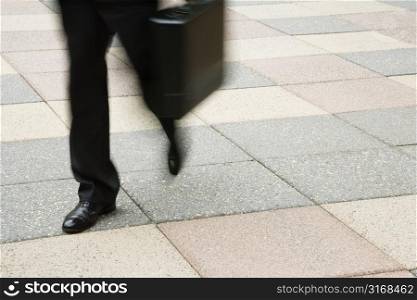 Motion blur of businessman legs walking outdoors with briefcase.