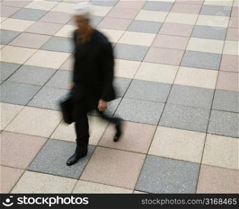 Motion blur of Caucasian businessman walking outdoors with briefcase.