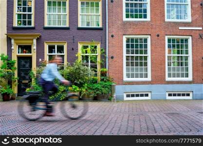Motion blurred bicycle rider cyclist man on bicycle very popular means of transport in Netherlands in street with old houses of Delft, Netherlands. Bicycle rider cyclist man on bicycle very popular means of transoirt in Netherlands in street of Delft, Netherlands