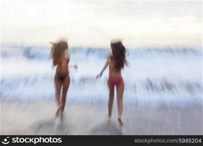Motion blurred photograph of young women girls in bikinis running on a beach