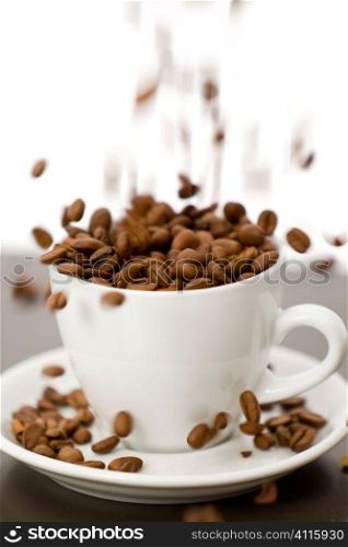 Motion blurred studio studio shot of coffee beans being poured into a white cup and saucer