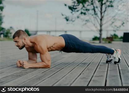 Motivated male athlete does abs exercise, enjoys bodybuilding training outdoor and stands in plank. Strong muscular European adult man has fitness workout. People and healthy lifestyle concept