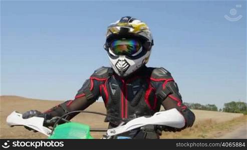 Motocross biker riding enduro motorcycle on country road front view medium shot