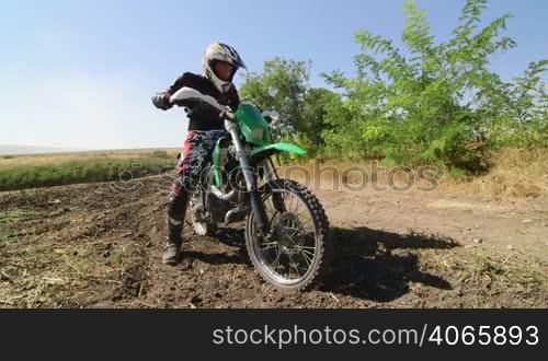 Motocross racer starting engine of his dirt bike riding away kicking up dust