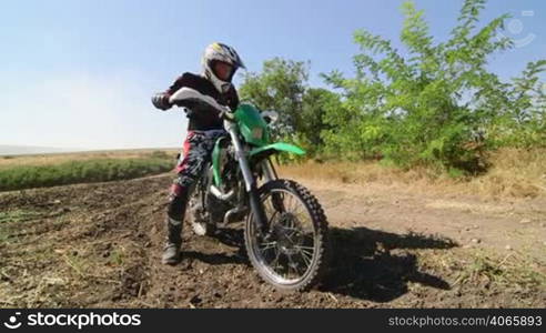 Motocross racer starting engine of his dirt bike riding away kicking up dust