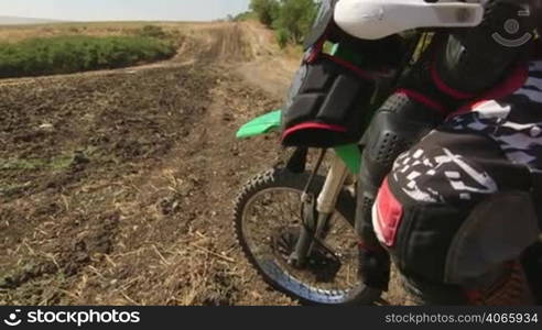 Motocross rider boy with his dirt bike looks afar jib crane shot