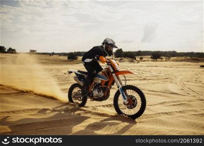 Motocross rider driving on sand dune further down off-road bike blowing dust from under wheel. Professional motocross rider driving on sand dune