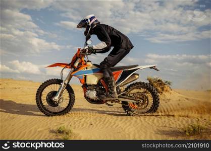 Motocross rider driving on sand dune further down off-road track blowing dust from under wheel. Professional motocross rider driving on sand dune