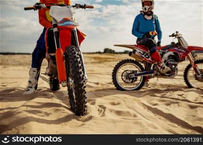 Motocross rider riders team rest on extreme desert terrain track. Focus on front iron horse wheel. Motocross riders team rest on extreme track
