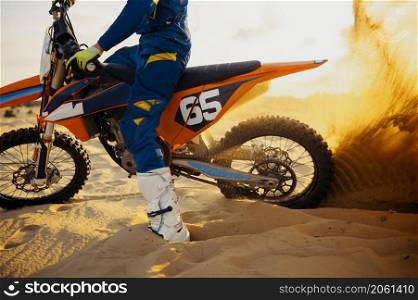 Motocross rider skidding wheel raising sand dust. Motocross riding, fast driving extreme activity. Motocross rider skidding wheel raising sand dust