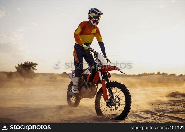 Motocross rider wearing protective helmet and suit on sport motor bike in desert. Motocross rider on sportmotor over dust landscape