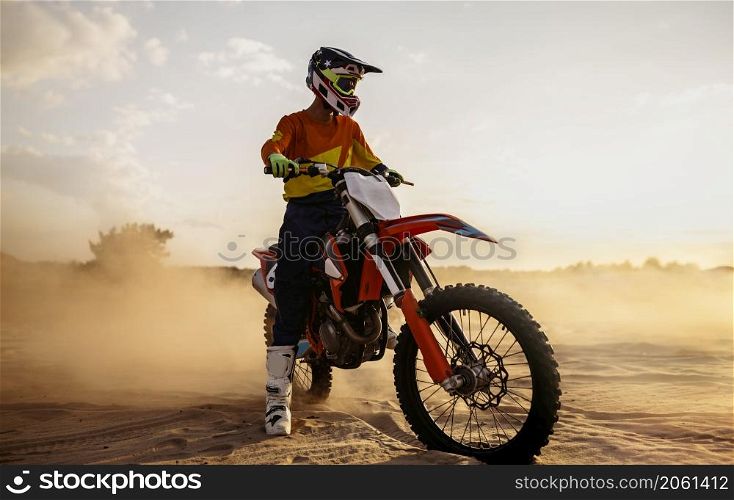 Motocross rider wearing protective helmet and suit on sport motor bike over dust landscape. Motocross rider on sportmotor over dust landscape