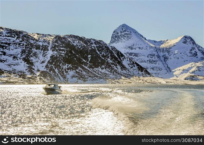 Motor boat in the middle of Nuuk fjord with frozen rocks in the background, Greenland
