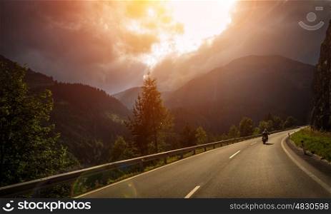 Motorcyclist in action, bright red sunset light, overcast weather, active lifestyle, traveling along Alpine mountains, extreme adventure concept