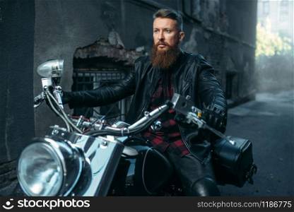 Motorcyclist in leather jacket poses on classical chopper. Vintage bike rider on motorcycle, freedom lifestyle. Motorcyclist in leather jacket poses on chopper