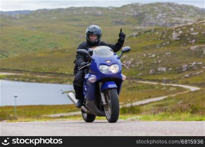 Motorcyclist in the Scottish Highlands, narrow road in mountain landscape