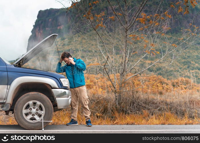 Motorist Broken Down On Country Road Phoning For Help. Asian man having trouble with his broken car