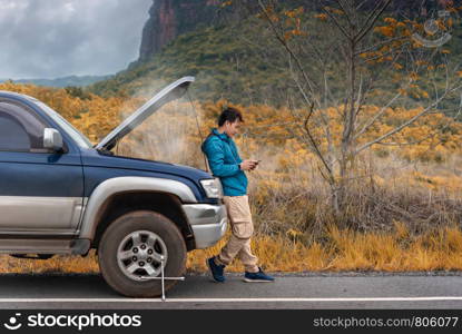 Motorist Broken Down On Country Road Phoning For Help. Asian man having trouble with his broken car