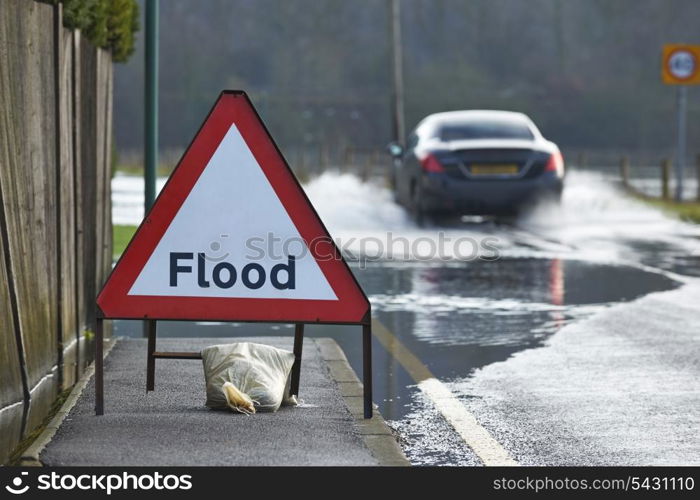 Motorist driving through flood waters with warning sign in foreground