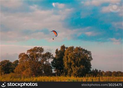 Motorized paraglider flying in rural area during sunset