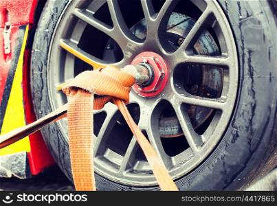 motosports, transportation and racing concept - close up of race car wheel with tow rope tied to it