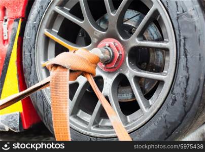 motosports, transportation and racing concept - close up of race car wheel with tow rope tied to it