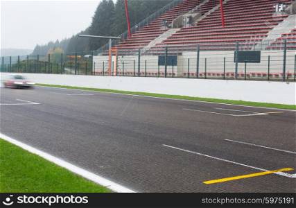 motosports, weather, extreme and race concept - close up of car driving on speedway track or road and stands under rain