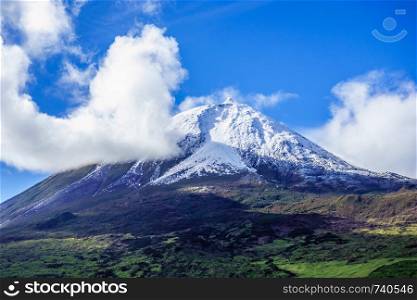 Mount Pico volcano summit covered in snow under blue sky and clouds, in Azores, Portugal.