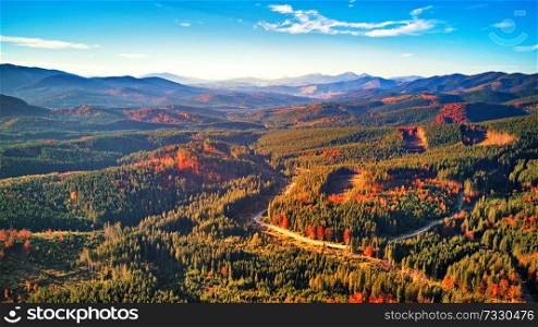 mountain autumn landscape with colorful forest. Road in fall season woodland with clouds and blue sky. Awesome alpine highlands in sunny day. Carpathian mountain valley