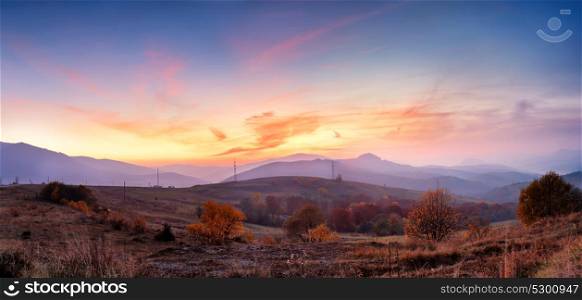 Mountain autumn panoramic landscape with colorful forest. Panorama of sunset in a Carpathian mountain valley with wonderful gold light on a hills. Panoramic image of rural fields in evening light