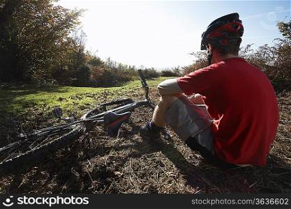 Mountain biker sitting beside bike in countryside