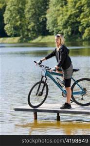 Mountain biking young woman standing on pier looking natural lake
