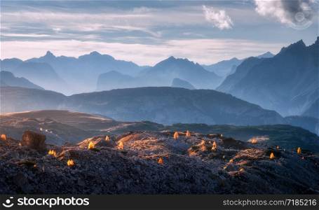 Mountain canyon lighted by bright sunbeams at sunset in autumn. Dolomites, Italy. Landscape with mountain ridges, rocks, colorful trees with orange leaves, alpine meadows, blue sky, sunlight in fall