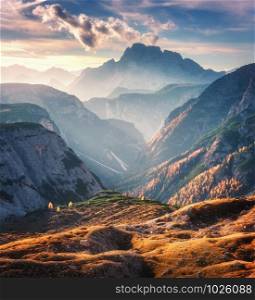 Mountain canyon lighted by bright sunbeams at sunset in autumn in Dolomites, Italy. Landscape with mountain ridges, rocks, colorful trees and orange grass, alpine meadows, gold sunlight in fall. Alps. Mountain canyon lighted by bright sunbeams at sunset in autumn