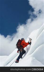 Mountain climber going up snowy slope with axes