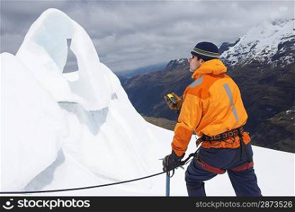 Mountain climber holding compass near ice formation in snowy mountains
