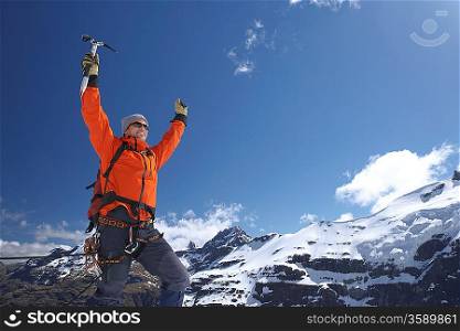 Mountain climber with arms raised on top of peak