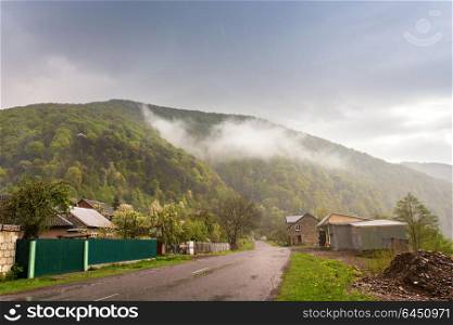 Mountain countryside. Road and village in green mountain valley. Spring stormy rainy weather