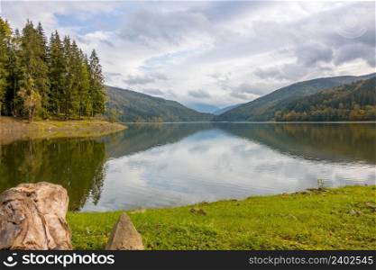 Mountain forest lake on a cloudy day. Clouds in the sky are reflected in the water surface. Clouds With Reflections in a Mountain Forest Lake