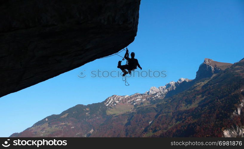 mountain guide on a large and overhanging roof lead and aid climbing a hard technical climb with a great background of blue sky and snow-capped peaks mountain landscape