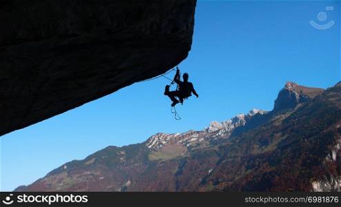 mountain guide on a large and overhanging roof lead and aid climbing a hard technical climb with a great background of blue sky and snow-capped peaks mountain landscape