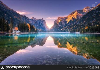 Mountain lake at sunrise in autumn. Landscape with lake, purple sky with gold sunlight, blue fog over the water, reflection, trees with colorful leaves, high rocks in fall. Forest in Dolomites, Italy. Lake in fog with reflection of mountains at sunrise in autumn