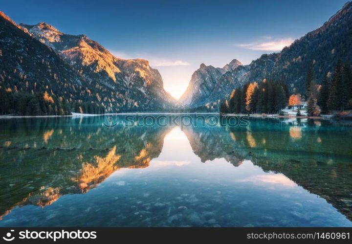 Mountain lake at sunset in autumn. Landscape with lake, blue sky with gold sunlight, reflection in water, trees with colorful leaves, high rocks in fall. Travel in Dolomites, Italy. Nature