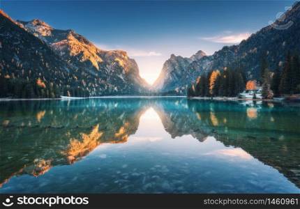 Mountain lake at sunset in autumn. Landscape with lake, blue sky with gold sunlight, reflection in water, trees with colorful leaves, high rocks in fall. Travel in Dolomites, Italy. Nature