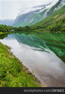Mountain lake with clean transparent water and rock reflection in still water surface (Norway, near Stordal). Summer cloudy view.