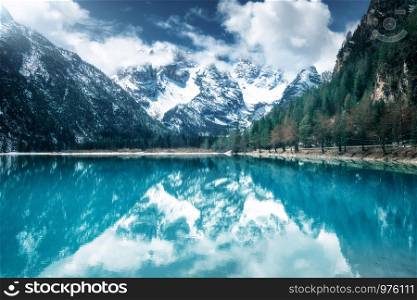 Mountain lake with perfect reflection at sunny day in autumn. Dolomites, Italy. Beautiful landscape with azure water, trees, snowy mountains in clouds, blue sky in fall. Snow covered rocks. Nature