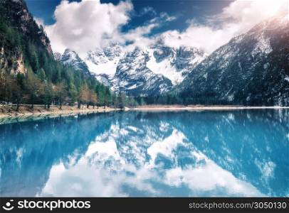 Mountain lake with perfect reflection at sunset in autumn. Dolomites, Italy. Beautiful landscape with azure water, trees, snowy mountains in clouds, blue sky in fall. Snow covered rocks. Nature