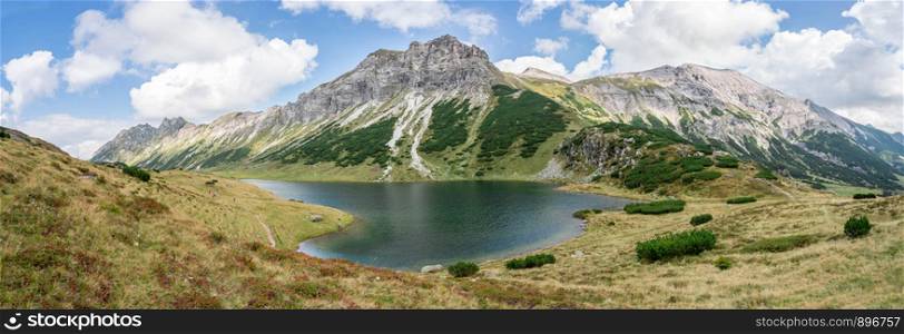 Mountain landscape: Rocky mountain range, clear water lake and blue cloudy sky; Panorama